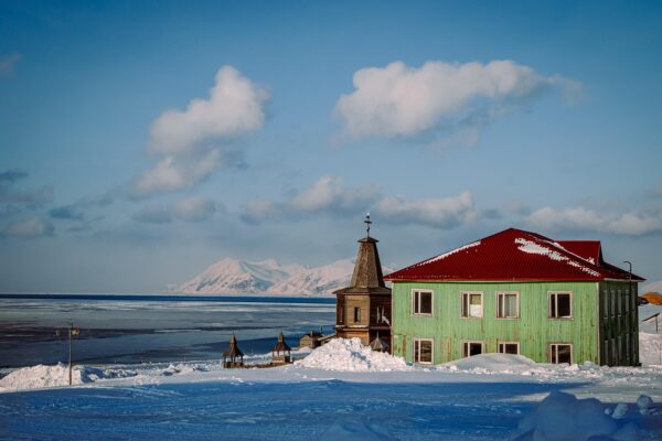 Vast sea ice stretches endlessly near Barentsburg in Svalbard with green building in forefront.